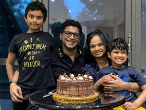 Lalitha with her husband and two sons posing in front of a birthday cake
