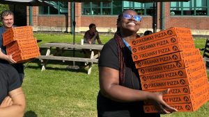 A staff member carries a tower of pizza boxes