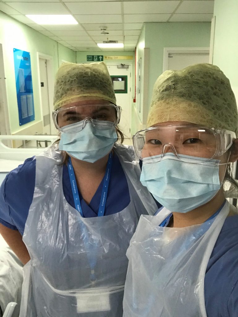 Julia and a colleague volunteering at St Mary's hospital. They are both wearing disposable scrubs, head coverings, masks and goggles