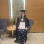 Leah Redmond seated in graduation attire, holding her Clinical Trichology Diploma certificate, smiling at the camera.