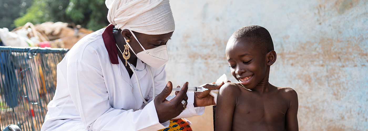 A young African boy receiving a vaccination from a female clinician.