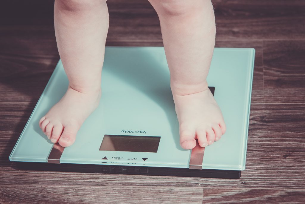 The legs of an overweight child standing on a set of digital scales. 