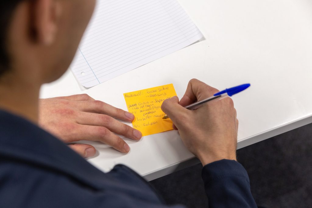 Person writes with pen on a yellow post-it note