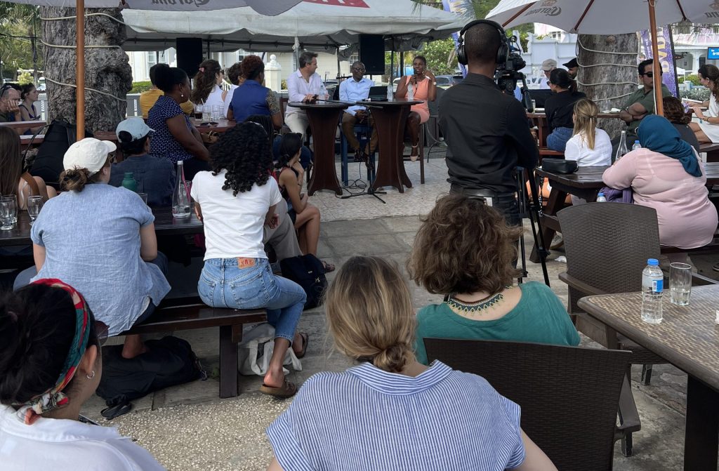 The CCM participants sit watching a panel discussion, outside at tables.