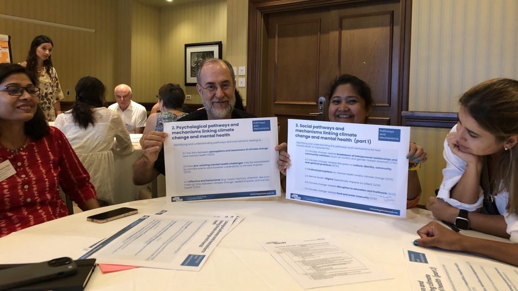 Sitting at a table for group work, two people hold up paper showing summary of research and action agendas