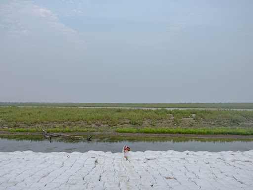 A woman returns home after collecting water from a nearby river, walking across large deposits of bags put together to protect the embankment from soil erosion due to the rising Brahmaputra river during peak monsoon season in Majuli island, Assam, India.