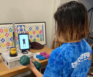 A woman holding dumbbells and looking at a tutorial on a phone