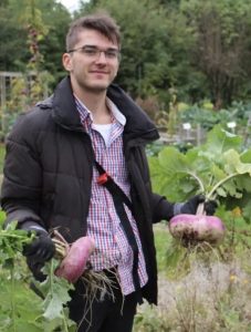 A man wearing a coat and glasses with two large turnips in his hands.