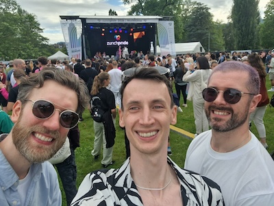 Three people smiling at a camera with an outdoor stage in the background