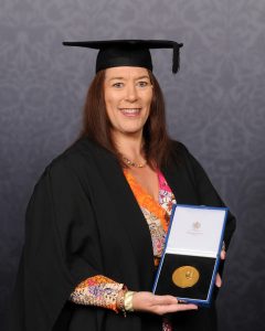 A woman wearing a graduation gown and holding a medal in a presentation box