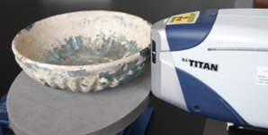 A handheld XRF analyser is pointed at a shallow cream and blue bowl. 