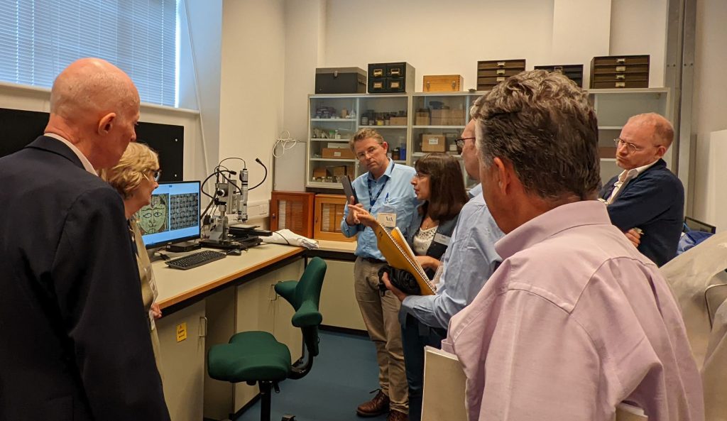 A group of researchers stands in a lab, looking at very high resolution microscope images on a screen.