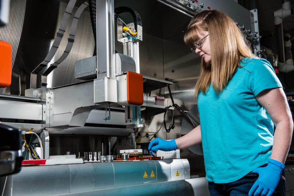 A researcher places a small sample vial into the autosampler for a laboratory robot. 