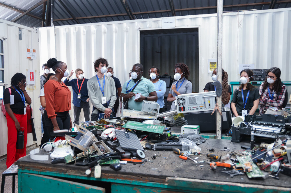 Students from Imperial and University of Nairobi, wearing protective masks, and observing a table filled with electronic waste.