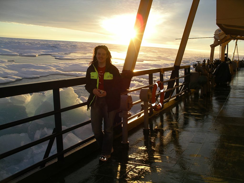 Cathy on a boat during her polar expedition, with the sun setting in the background