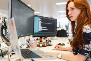 an employee sitting in front of two desktop displays with lines of code