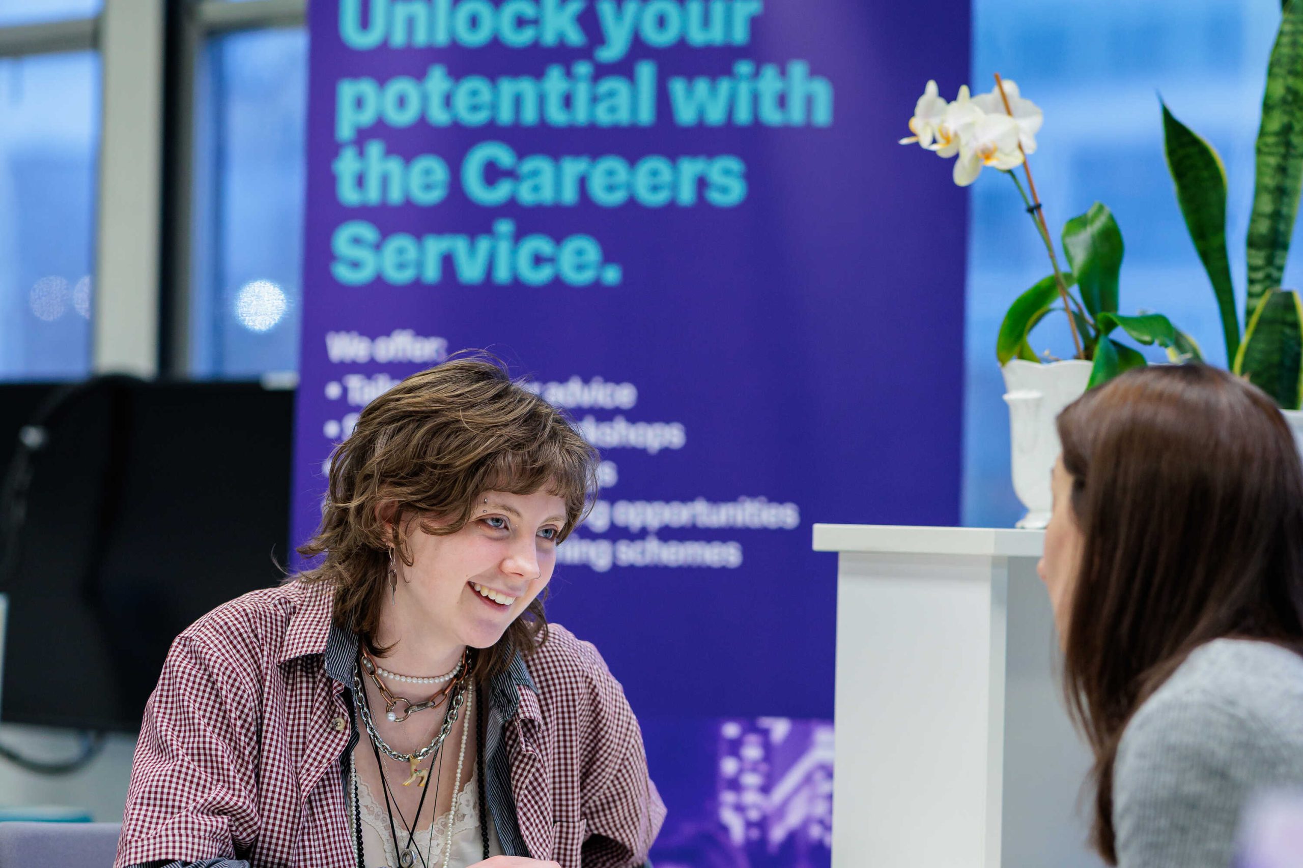 Two people talking with a pop-up banner behind them saying "Unlock your potential with the Careers Service"