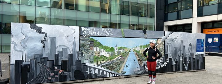 Judy standing next to a large painted mural on Imperial's South Kensington Campus, saying 'Innovate with purpose, sustain with care'